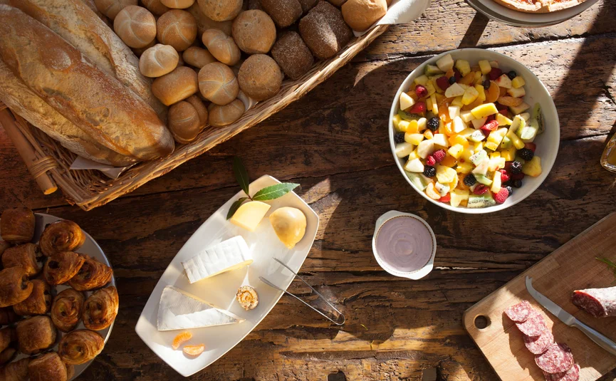 Tisch mit Brot, Käse, Aufschnitt und Obstsalat auf rustikalem Holz