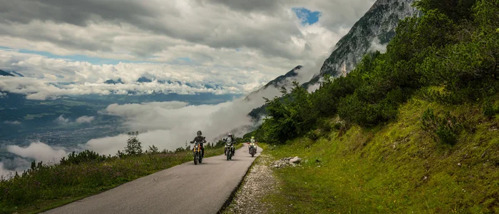 Drei Motorräder fahren auf einer Bergstraße mit Wolken und grüner Landschaft