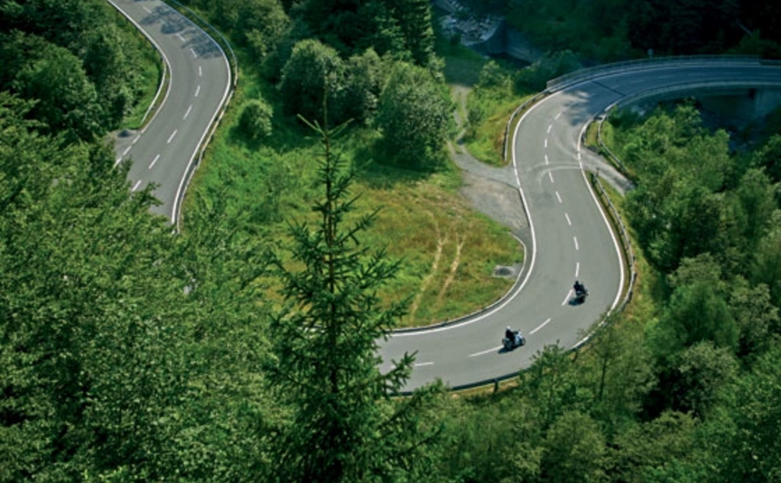 Kronkelende bergweg met twee motorfietsen omgeven door groene bomen