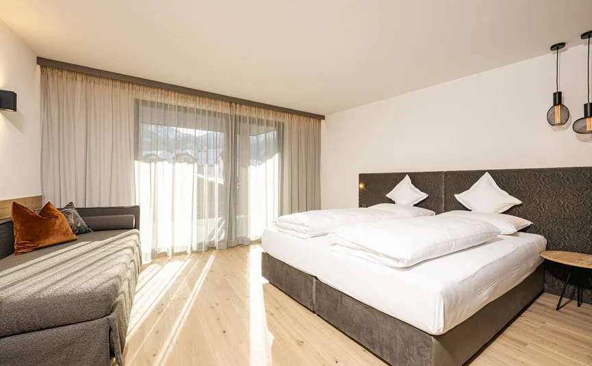 Brightly lit bedroom with double bed and sofa by large window