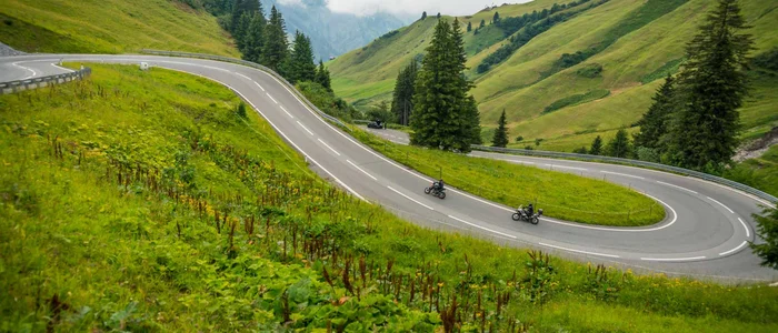Winding mountain road with two motorcyclists and green hills