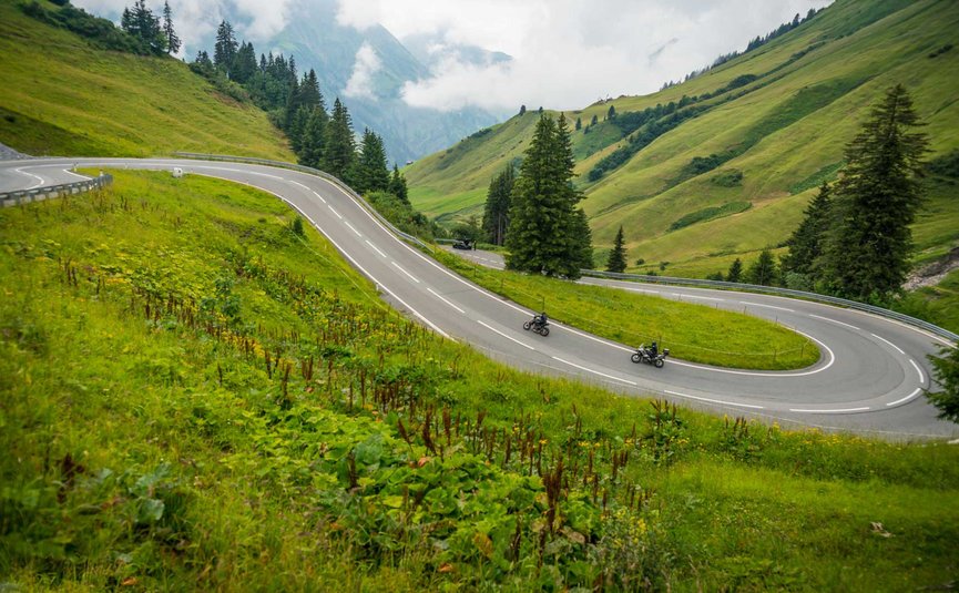 Kronkelende bergrivier met twee motorrijders en groene heuvels