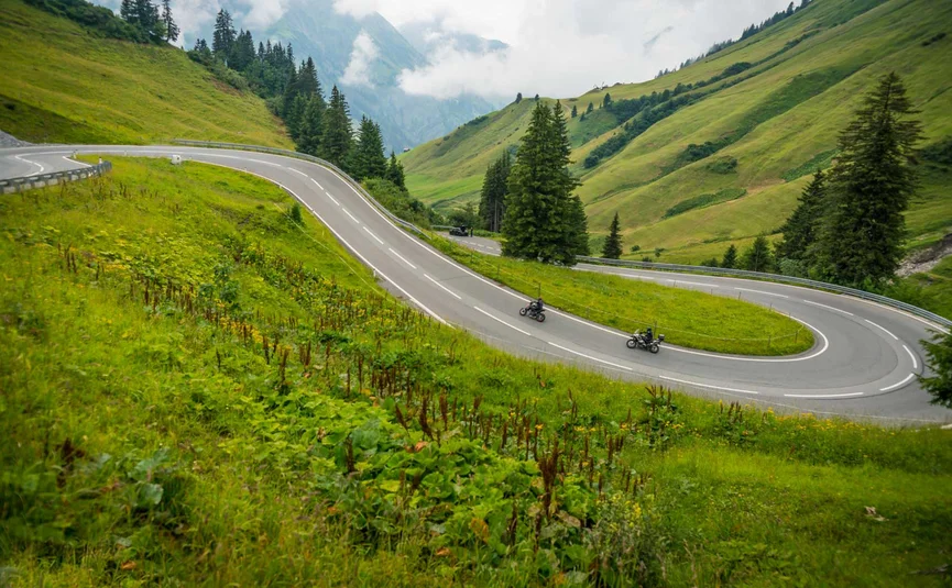 Motorradurlaub im Lechtal – Hahntennjoch © Moppetfoto.de Kurvige Bergstraße mit zwei Motorradfahrern und grünen Hügeln