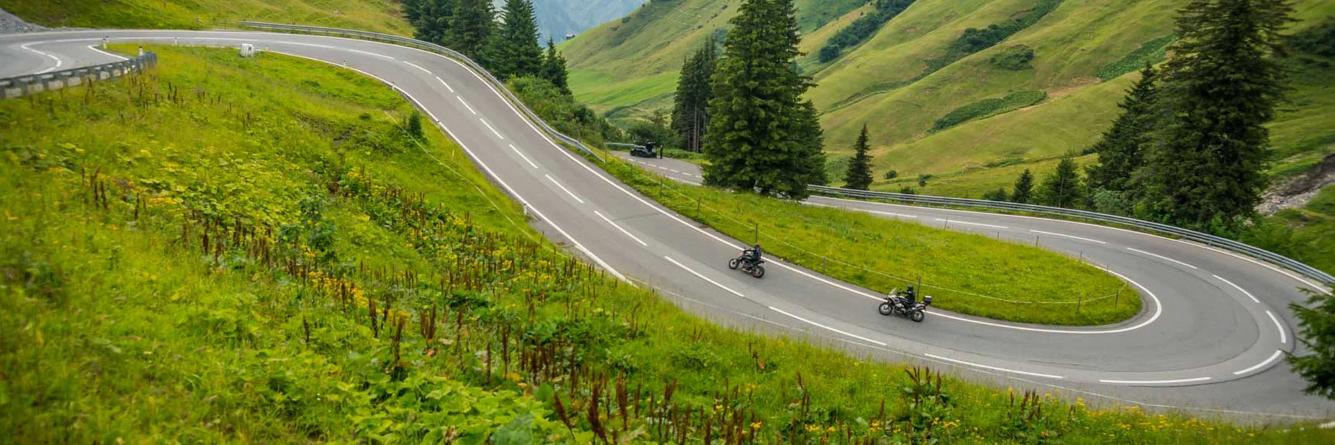 Winding mountain road with two motorcyclists and green hills