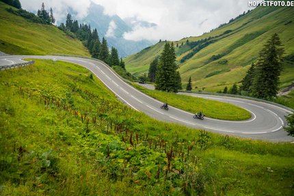 Kurvige Bergstraße mit zwei Motorradfahrern und grünen Hügeln