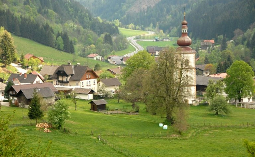 Kleines Dorf mit Kirche und grünen Feldern in einem Bergtal