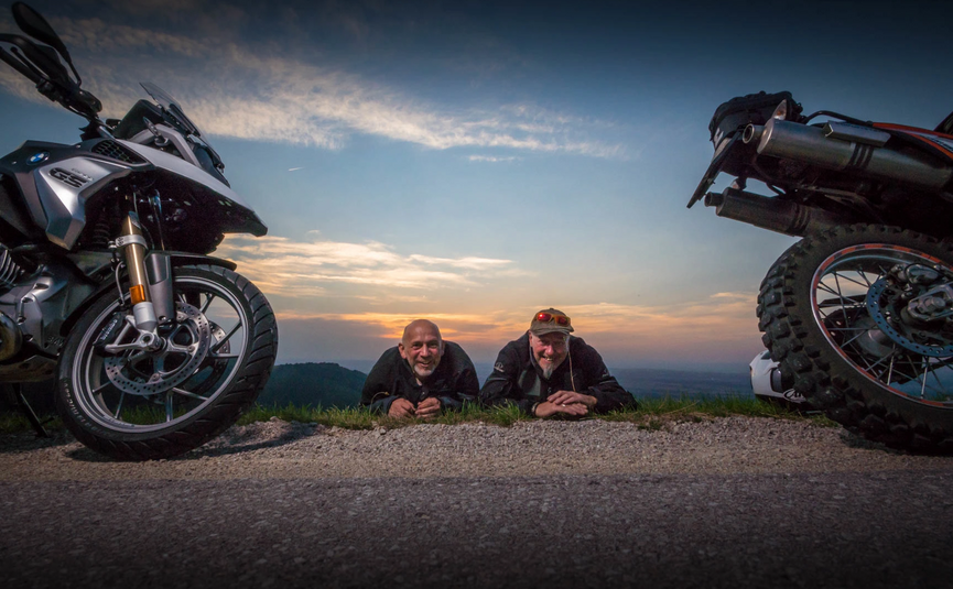Henpstpass Tour 368km Two men lying on road between motorcycles at sunset