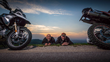 Henpstpass Tour 368km Zwei Männer liegen zwischen Motorrädern bei Sonnenuntergang auf einer Straße