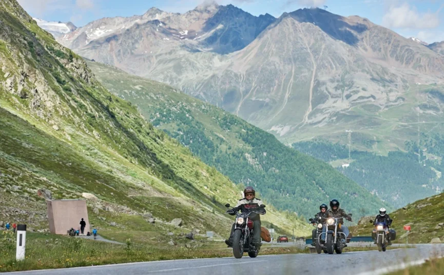 Grensland tour Motorfietsers rijden op bergweg met Alpen op de achtergrond bij helder weer