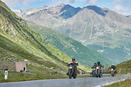 Motorradfahrer auf Bergstraße mit Alpen im Hintergrund bei klarem Wetter