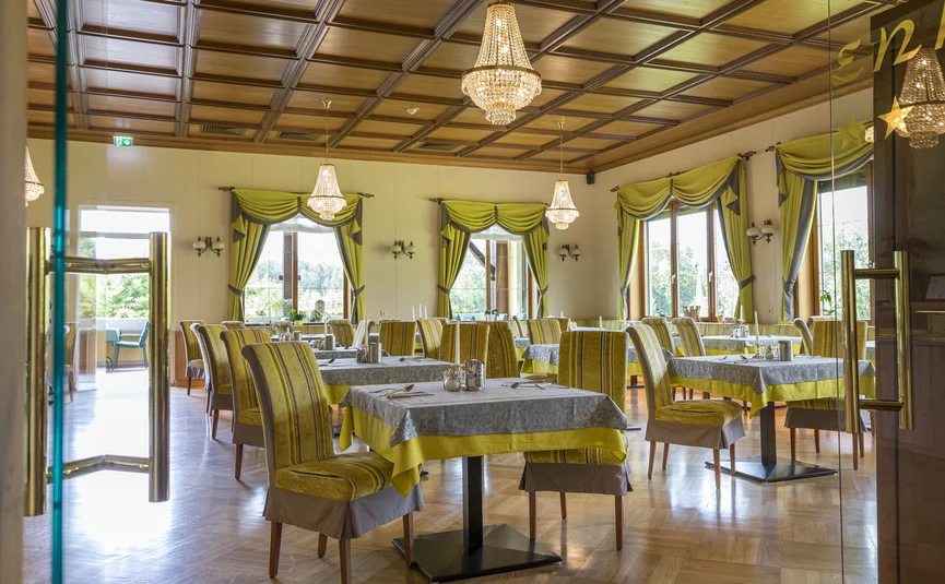 Elegant restaurant met houten panelen, kroonluchters en geel-groene gordijnen