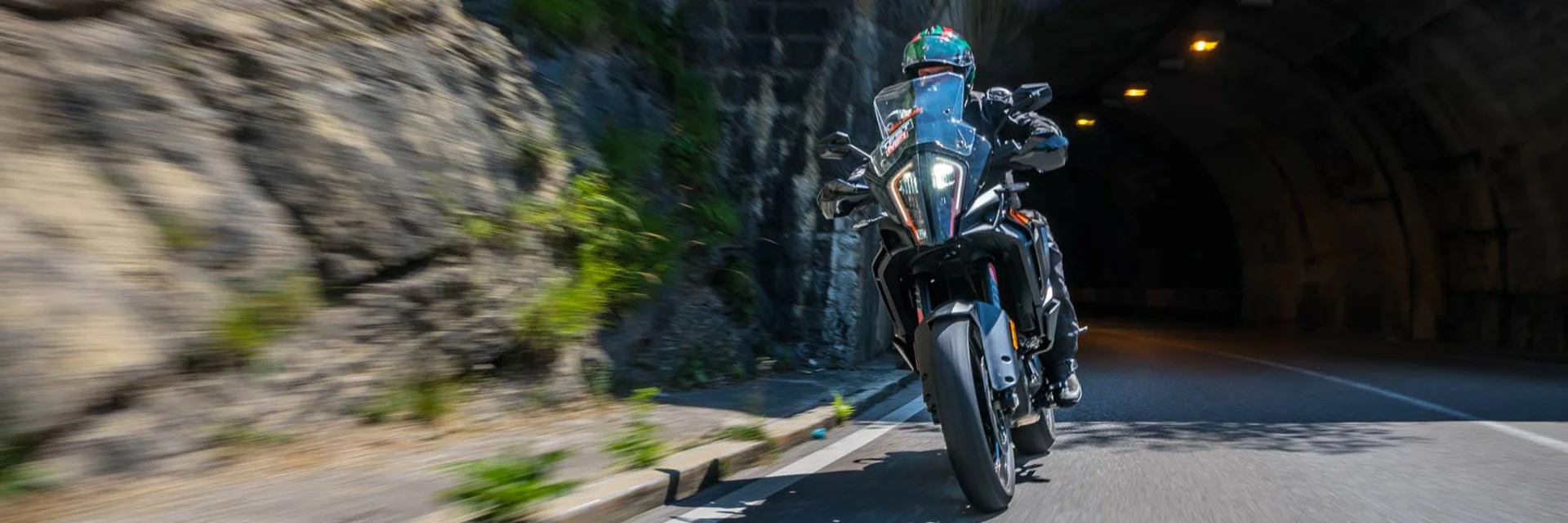 Motorcyclist riding through a tunnel beside a rocky wall