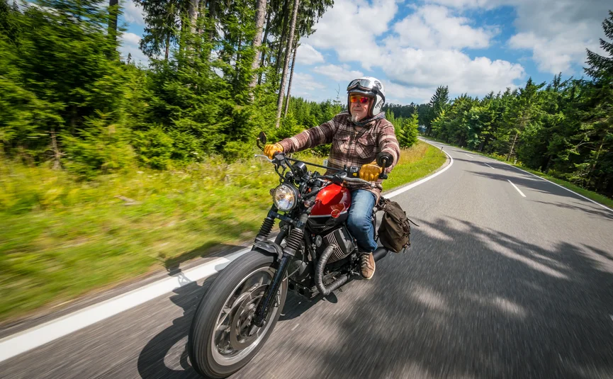 Older man riding motorcycle on winding forest road in daylight