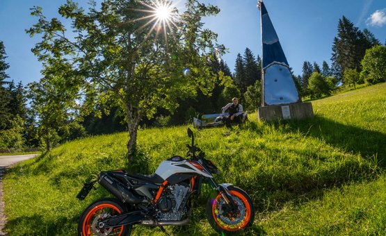 Motorrad auf grüner Wiese mit Baum und Person im Hintergrund bei Sonnenschein