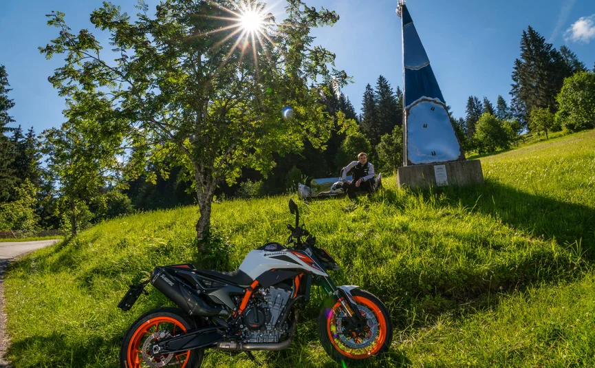 Motorrad auf grüner Wiese mit Baum und Person im Hintergrund bei Sonnenschein