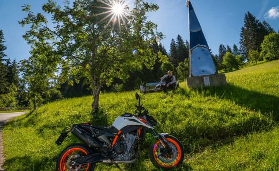 Motorfiets op groen weiland met boom en persoon op achtergrond in zonlicht