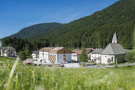 Dorf mit Kirche und Bergen im Hintergrund bei sonnigem Himmel