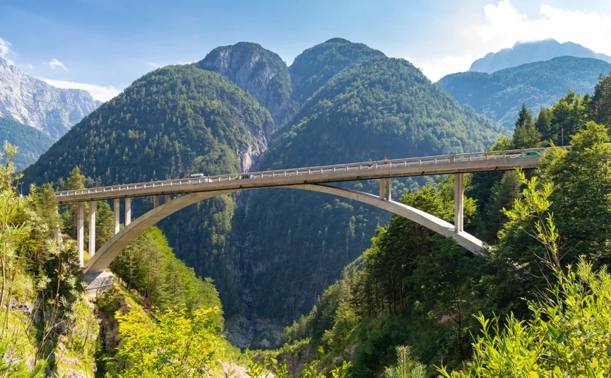 Concrete arch bridge over green valley with forested mountains