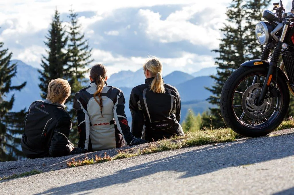 Three motorcyclists sitting on a hill with mountain scenery in the background