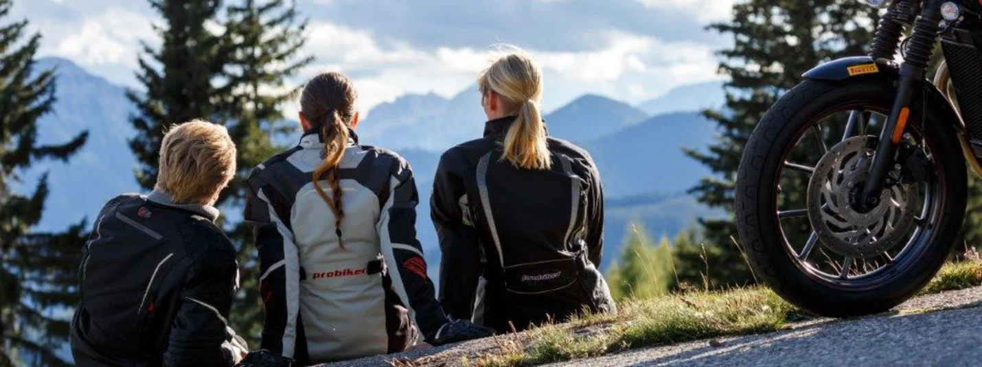 Three motorcyclists sitting on a hill with mountain scenery in the background