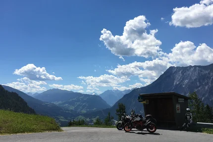 Motorcycles parked by a bus stop with mountains and cloudy sky