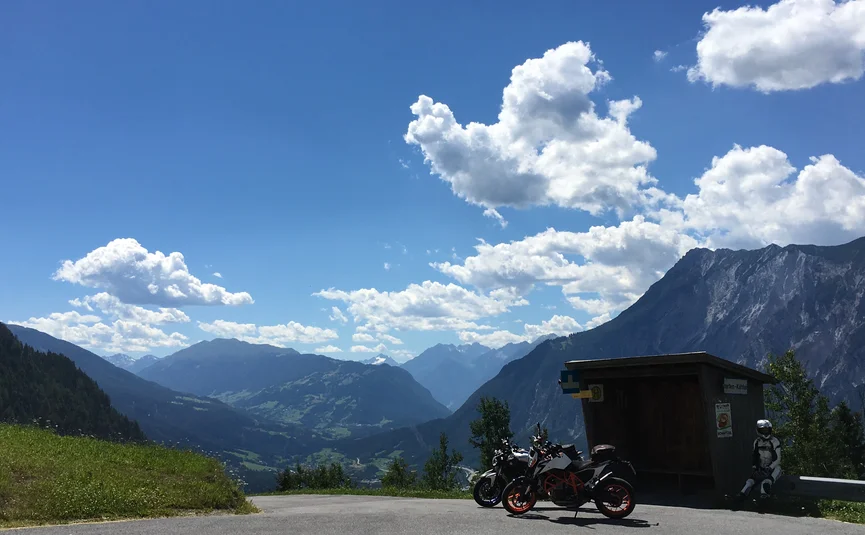 11 Hotel Sonnleiten: Jachenau Kühtai Gnadenwald Motoren geparkeerd bij bushalte met bergen en bewolkte lucht