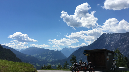 Motorräder vor einer Bushaltestelle mit Bergblick und bewölktem Himmel