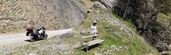 Motorradurlaub im Grenzgebiet Oststeiermark-Südburgenland © Leberzipf Didi Motorradfahrer steht neben Bank und Motorrad an Bergstraße bei Felswand