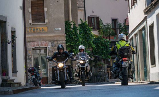 Motorradurlaub in Friaul – Julisch Venetien © Moppetfoto.de Motorradfahrer fahren durch eine ruhige Stadtstraße mit alten Gebäuden
