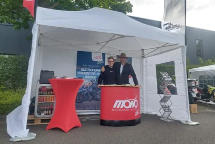 Twee personen bij een MoHo Motorrad Hotels kraam onder een witte tent