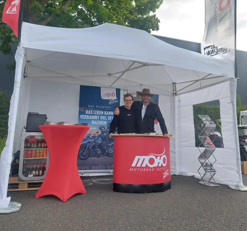 40 Jahre Wunderlich Zwei Personen an einem MoHo Motorrad Hotels Stand unter weißem Zelt