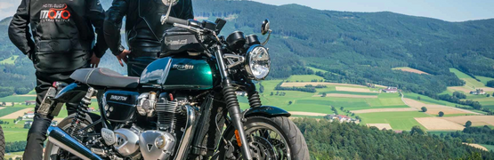 Steirische Satteltour Zwei Motorradfahrer mit Triumph Thruxton vor Berg- und Wiesenaussicht