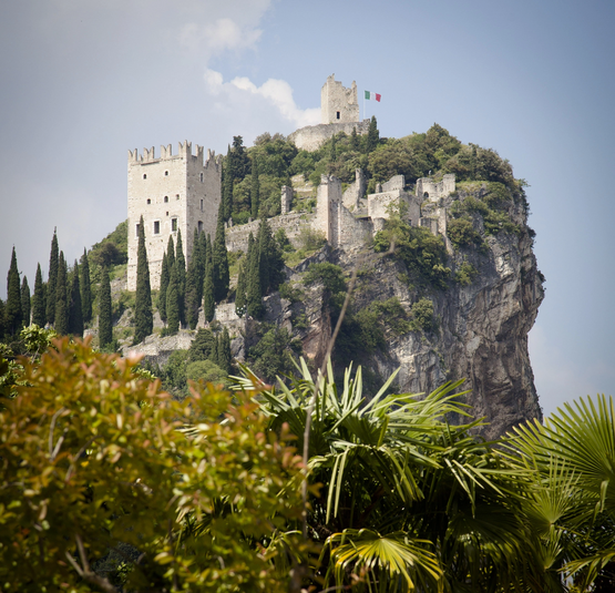 Burgruine auf einem bewaldeten Felsen mit italienischer Flagge