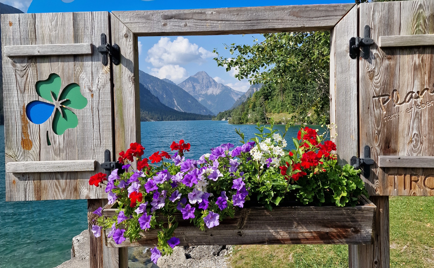 Blick auf See und Berge durch dekorativen Holzrahmen mit Blumen