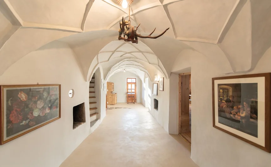 Bright corridor with white plaster walls, Gothic vault ceiling, and framed pictures