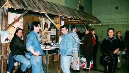 Menschen unterhalten sich an einem Holzhüttenstand in einer Halle
