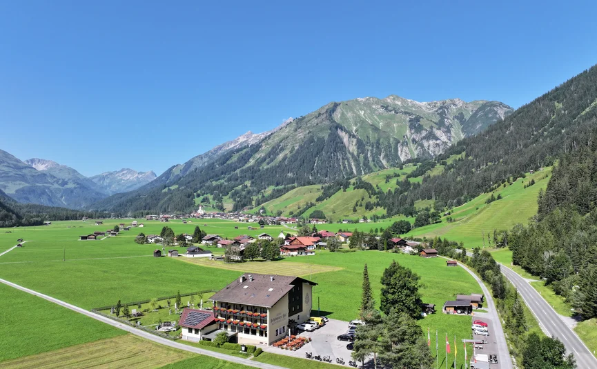 View of a hotel in a green valley with mountains under clear blue sky