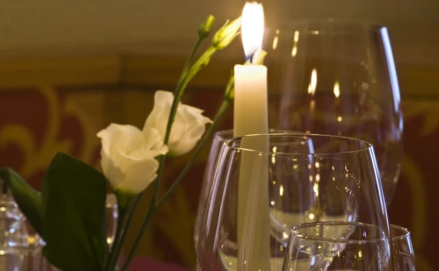Stressfreier Advent. Genießen statt hetzen. Brennende Kerze und Weingläser auf einem gedeckten Tisch mit Blumen
