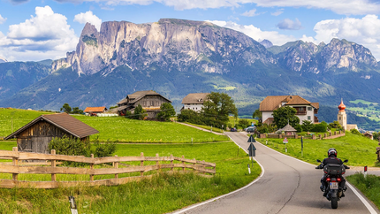 Motorrijder op landweg met Alpen en boerderijen op achtergrond