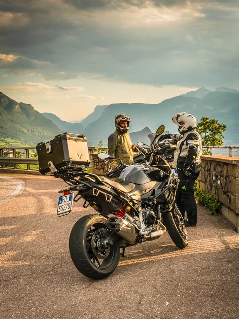 Two motorcyclists with their bikes on mountain road at sunset