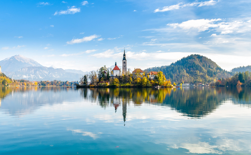 Kircheninsel auf einem ruhigen See mit Bergen und blauem Himmel im Hintergrund