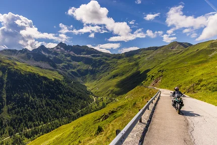 Motorcyclist on mountain road overlooking green valleys and mountains