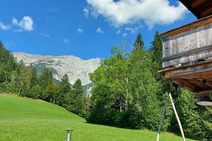 Green hillside with forest and cloudy sky next to wooden cabin
