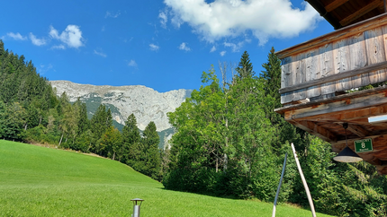 Grüner Berghang mit Wald und Wolkenhimmel neben Holzhütte