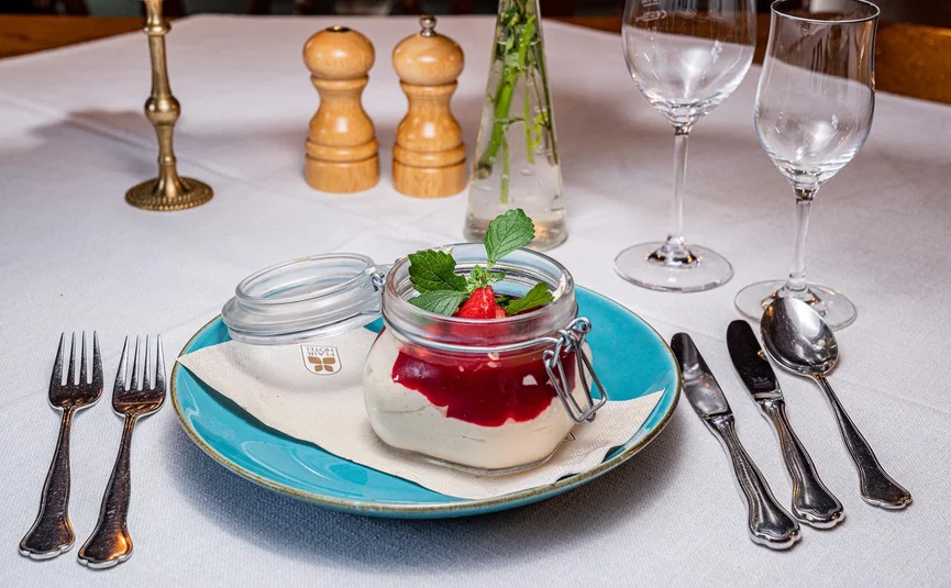 Dessert in glass jar with strawberry sauce and mint leaf on blue plate