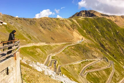 Person looking at winding mountain road with mountains and blue sky