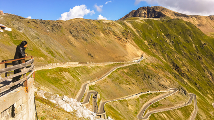 Person blickt auf kurvenreiche Bergstraße mit Bergen und blauem Himmel