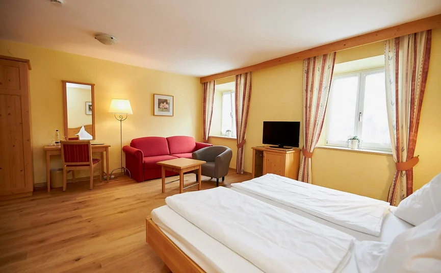 Bright hotel room with double bed, red sofa, desk, and TV