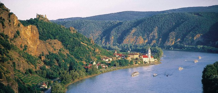 Fluss mit Booten, Hügeln und einem Dorf mit historischen Gebäuden