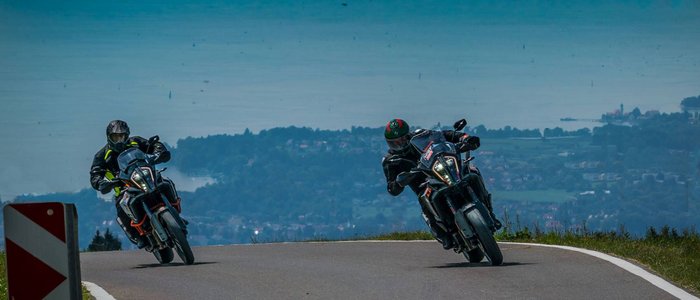 Zwei Motorradfahrer fahren eine kurvige Bergstraße mit Seeblick